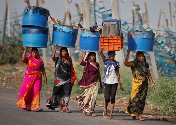 نساء يحملن متعلقاتهن بعد إنقاذهن من أماكن عملهن المتضررة في ميناء صيد بعد إعصار تاوكتاي في جافراباد في ولاية غوجارات الغربية، الهند، 19 مايو 2021 - سبوتنيك عربي