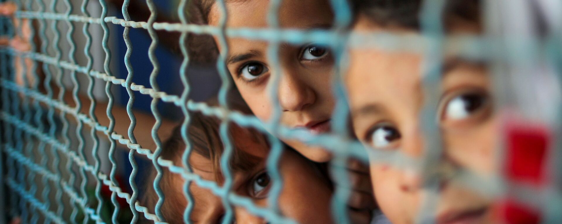 أطفال ينظرون من نافذة مدرسة الأنروا. يذكر أنه نزح ما يقرب 34 ألف من أهالي قطاع غزة إلى مدراس الأونروا بعد قصف الطيران الحربي الإسرائيلي منازلهم، فلسطين بتاريخ 18 مايو 2021 - سبوتنيك عربي, 1920, 31.07.2021