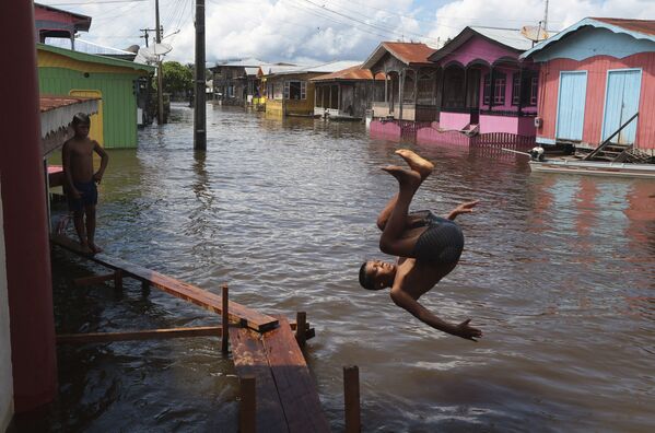 صبي يقفز في شارع غمرته المياه في أناما، ولاية أمازوناس، البرازيل، 14 مايو 2021. - سبوتنيك عربي