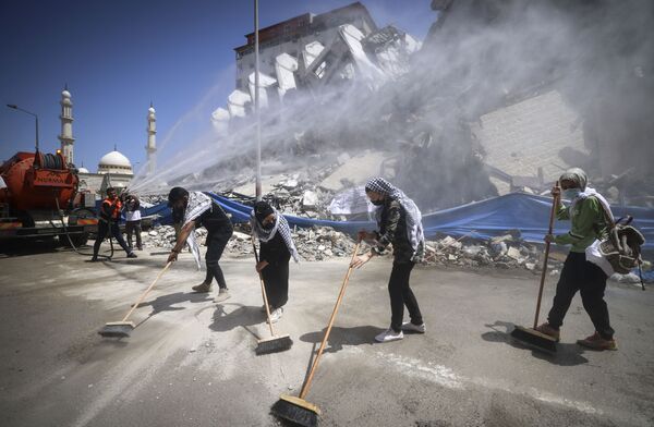 متطوعون فلسطينيون وعمال بلدية يقومون بإزالة أنقاض مجمع برج هنادي، الذي دمرته الغارات الإسرائيلية في الحرب الأخيرة، في حي الرمال بمدينة غزة، في 25 مايو 2021 - سبوتنيك عربي