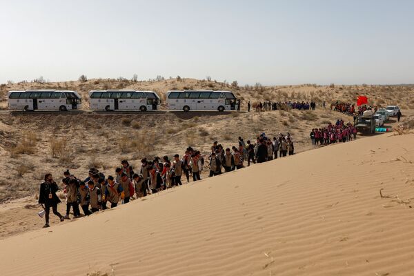 أطفال يسيرون على طول الكثبان الرملية أثناء فعالية لزرع طوعي للأشجار نظمته مدرستهم على حافة صحراء غوبي في ضواحي ووي، مقاطعة غانسو، الصين 16 أبريل 2021 - سبوتنيك عربي