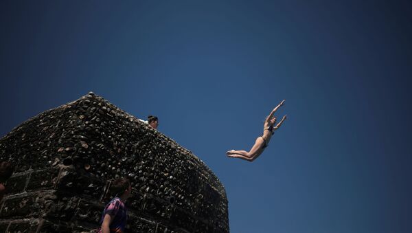 فتاة تقفز إلى مياه البحر حيث يستمتع الناس بالطقس الحار على شاطئ برايتون في برايتون، بريطانيا، 1 يونيو 2021 - سبوتنيك عربي