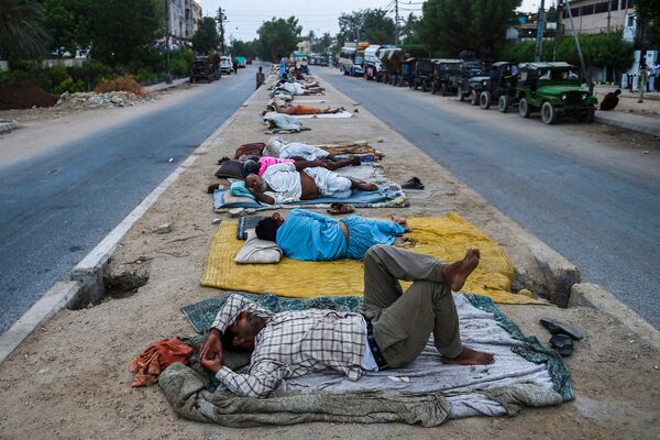 عمال ينامون على حاجز طريق وسط شارع في مدينة كراتشي الساحلية، باكستان في 1 يونيو 2021 - سبوتنيك عربي