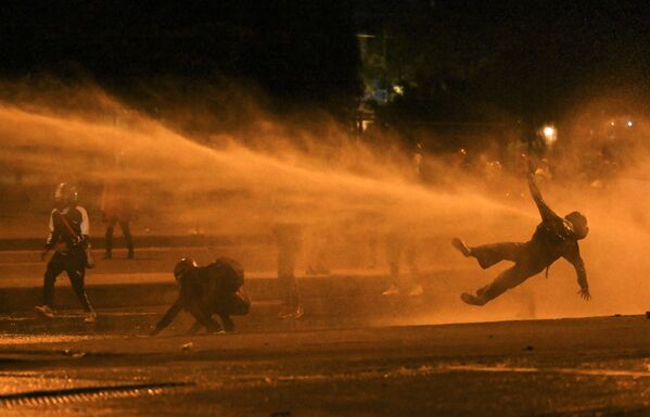 سقوط أحد المتظاهرين جراء إصابتهم بخراطيم المياه ، خلال اشتباكات مع شرطة مكافحة الشغب وسط احتجاجات مستمرة ضد حكومة الرئيس الكولومبي إيفان دوكي في بوغوتا، 12 يونيو 2021 - سبوتنيك عربي
