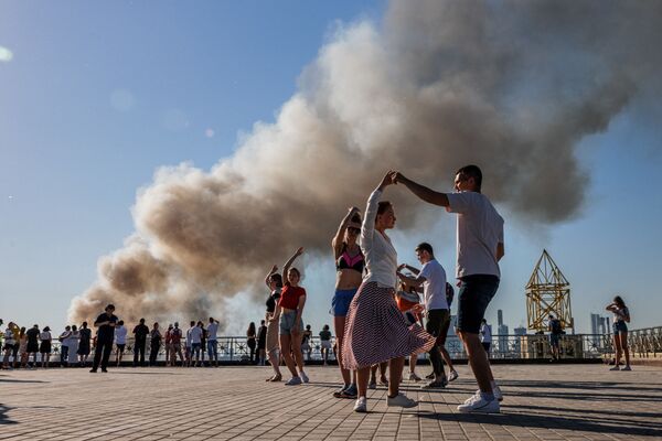 أزواج يرقصون السامبا بينما يتصاعد الدخان من مستودع للألعاب النارية مشتعل في موسكو، روسيا 19 يونيو 2021 - سبوتنيك عربي
