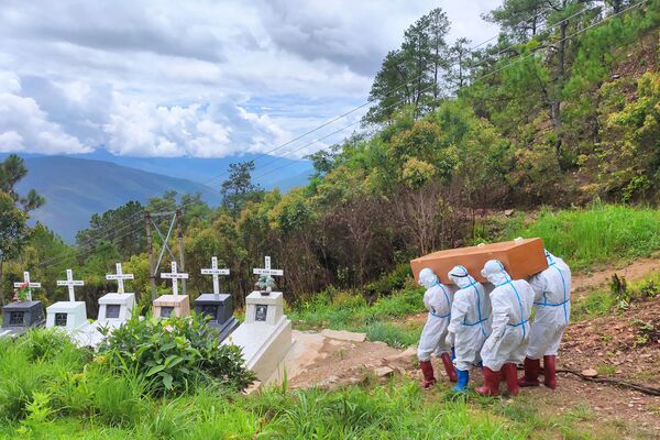تُظهر هذه الصورة المنشورة من مجموعة تشينلاند هيرالد دايلي نيوز الإعلامية المحلية التي تم التقاطها في 21 يونيو 2021 وتم إصدارها في 22 يونيو، موظفون في القطاع الصحي يرتدون بدلة واقية ويحملون نعشًا لجثة مريض كوفيد-19، أثناء دفنه في مقبرة في فالام بلدة في ولاية تشين غرب ميانمار. - سبوتنيك عربي