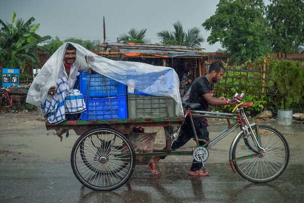 رجل يلف ملاءة بلاستيكية ليحتمي بها من المطر، أثناء جلوسه على عربة دراجة أثناء هطول أمطار غزيرة في دكا، بنغلادش 21 يونيو 2021 - سبوتنيك عربي
