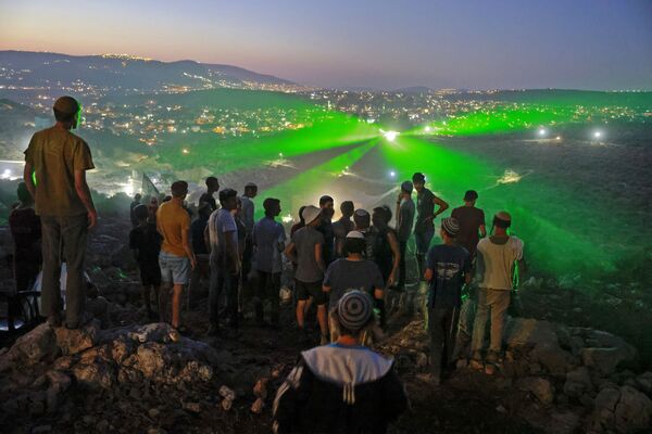المستوطنون الإسرائيليون والمناصرين لإسرائيل يقفون في موقع استيطاني الذي أُنشئ حديثًا في إيفياتار، ينظرون إلى المتظاهرين الفلسطينيين الذين يضيئون بأشعة الليزر باللون الأخضر باتجاههم من قرية بيتا القريبة منهم، بالقرب من مدينة نابلس، في الضفة الغربية، 28 يونيو 2021 - سبوتنيك عربي