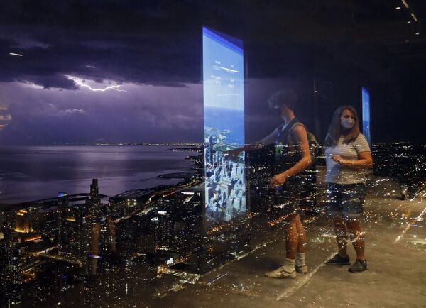 انعكاس الأشخاص على جدار زجاجي لبرج ويليس، حيث يومض البرق عبر السماء بالقرب من بحيرة ميشيغان، في شيكاغو الأمريكية  29 يونيو 2021 - سبوتنيك عربي