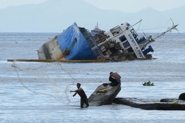 صياد يلقي شبكته على خلفية سفينة إم/ في بالاوان بيرل نصف المغمورة بعد اصطدامها في خليج مانيلا في الفلبين، 8 يوليو 2021 - سبوتنيك عربي