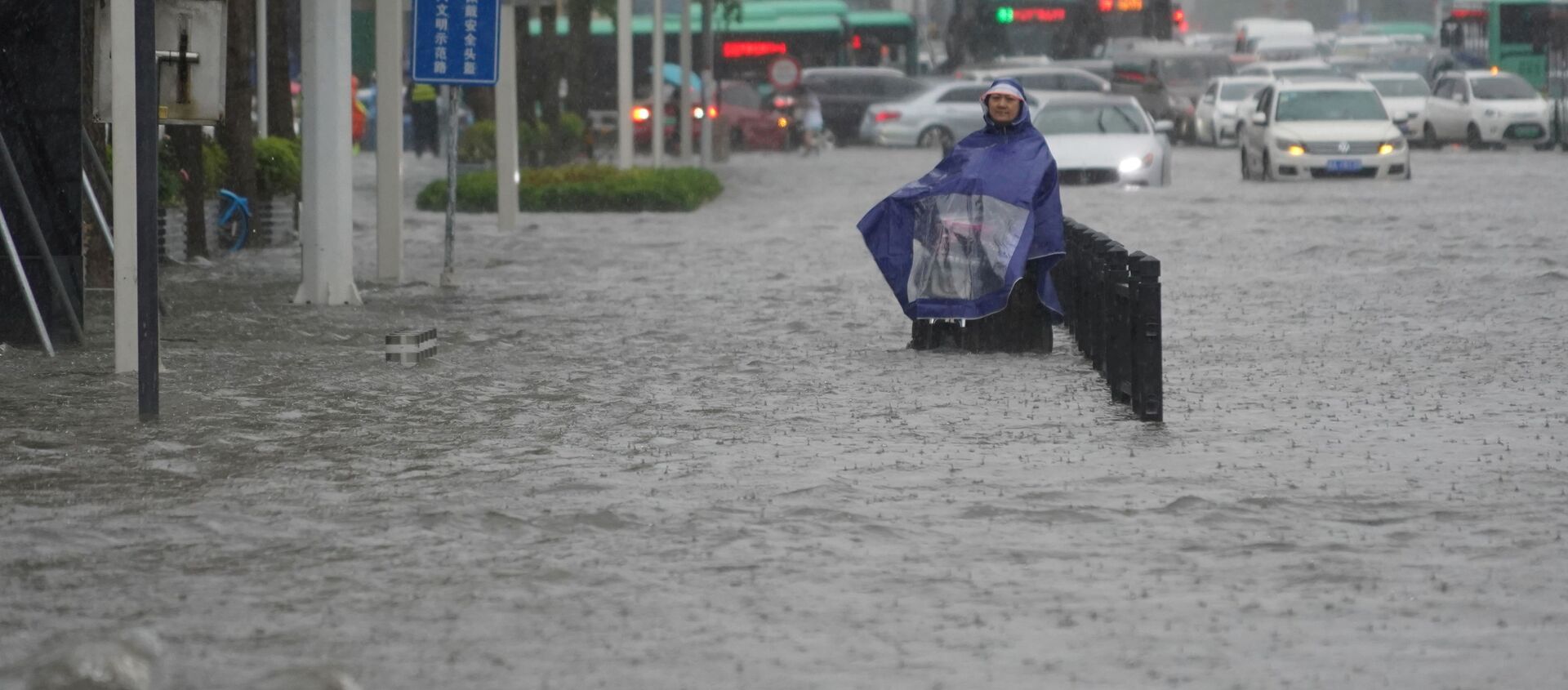 ساكن يرتدي غطاء مطر يقف على طريق غمرته المياه في مدينة تشنغتشو بمقاطعة خنان الصينية 20 يوليو 2021 - سبوتنيك عربي, 1920, 21.07.2021