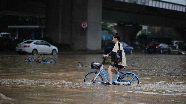 فتاة تعبر الشارع بواسطة دراجتها في أحد شوارع مدينة تشنغتشو التي غمرتها مياه الفيضانات، وسط محافظة هينان، الصين 22 يوليو 2021 - سبوتنيك عربي
