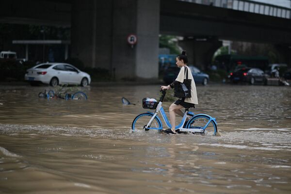 فتاة تعبر الشارع بواسطة دراجتها في أحد شوارع مدينة تشنغتشو التي غمرتها مياه الفيضانات، وسط محافظة هينان، الصين 22 يوليو 2021 - سبوتنيك عربي