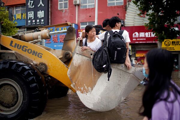 أشخاص يركبون جرافة في طريق غمرته مياه الفيضانات في مدينة تشنغتشو بمقاطعة هينان، الصين 22 يوليو 2021 - سبوتنيك عربي