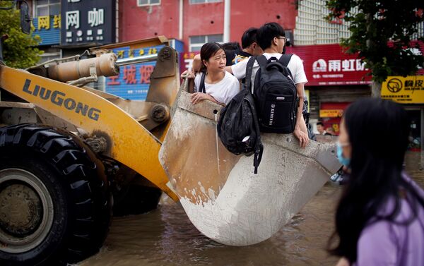 أشخاص يركبون جرافة في طريق غمرته مياه الفيضانات في مدينة تشنغتشو بمقاطعة هينان، الصين 22 يوليو 2021 - سبوتنيك عربي