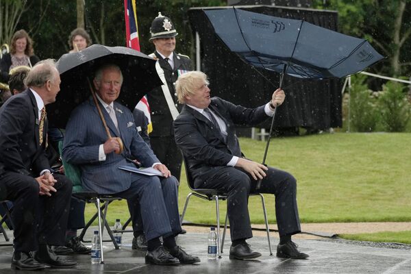 الأمير تشارلز، وسط الصورة، ورئيس الوزراء بوريس جونسون، إلى اليمين، يحتميان من المطر أثناء إزاحة الستار عن النصب التذكاري لشرطة المملكة المتحدة في بستان النصب التذكاري الوطني في ألريواس، إنجلترا، 28 يوليو 2021 - سبوتنيك عربي