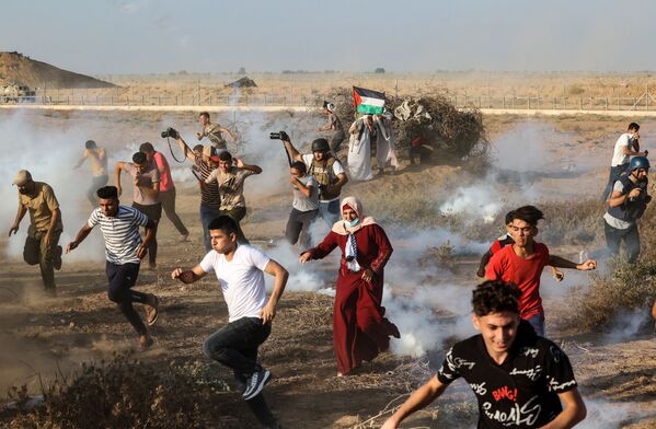 متظاهرون فلسطينيون وصحفيون يفرون من قنابل غاز المسيلة للدموع على حدودو قطاع غزة، فلسطين 25 أغسطس 2021 - سبوتنيك عربي