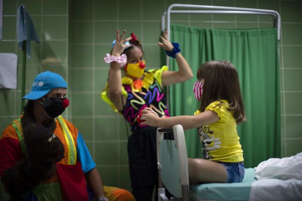 المهرجون يقومون بترفيه فتاة أثناء انتظارها في غرفة التمريض بعد حقنها بجرعة من لقاح سوبيرانا-02 ضد كوفيد-19 في هافانا، كوبا،  24 أغسطس 2021 - سبوتنيك عربي