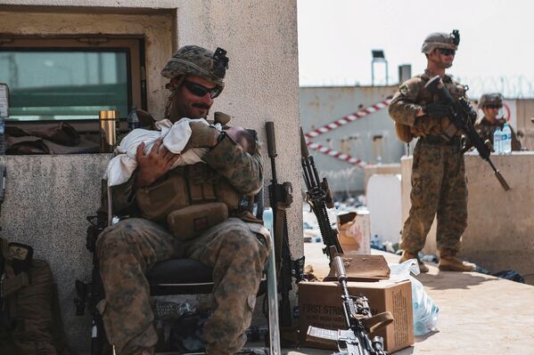 جندي من مشاة البحرية الأمريكية تم تعيينه في الوحدة الاستكشافية البحرية الرابعة والعشرين، يحمل طفلاً أثناء عملية إجلاء الأفغانيين في مطار حامد كرزاي الدولي في كابول، أفغانستان، 20 أغسطس 2021 - سبوتنيك عربي