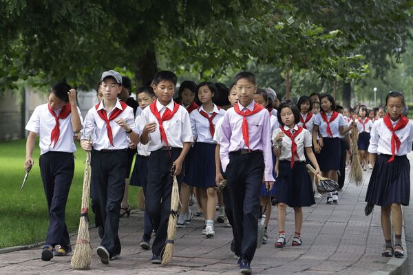 يحمل أطفال المدارس المكانس أثناء سيرهم إلى أماكن عامة مختلفة لتنظيف العشب وإزالة الأعشاب منه في محاولة للحفاظ على نظافة المدينة، في بيونغ يانغ، كوريا الشمالية 28 يوليو 2017 - سبوتنيك عربي