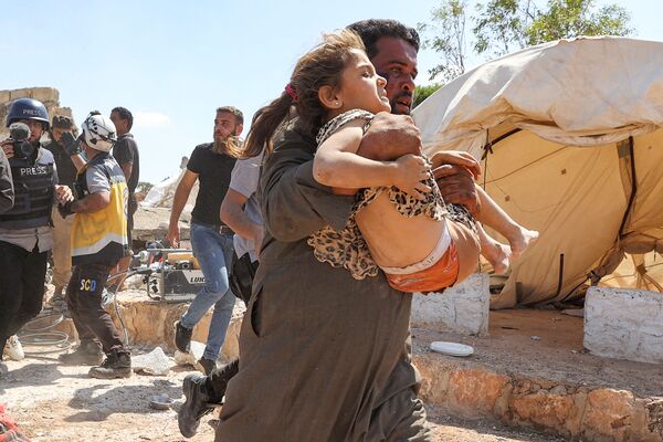 رجل يحمل فتاة أصيبت بجروح خلال قصف جوي على مخيم مؤقت للنازحين السوريين بالقرب من بلدة كفريا، شمال محافظة إدلب، سوريا 7 سبتمبر 2021 - سبوتنيك عربي
