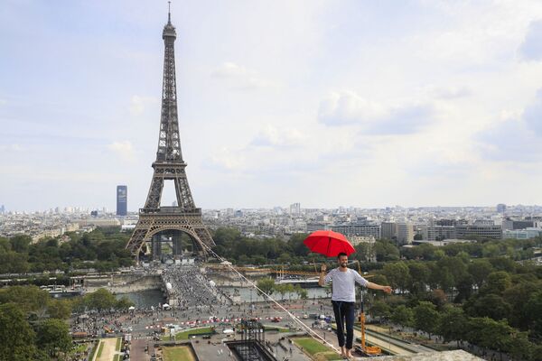 الفرنسي ناثان بولين يحمل مظلة وهو يسير، للمرة الثانية، على حبل مشدود بارتفاع 70 مترًا يمتد 670 مترًا بين برج إيفل ومسرح شايو الوطني، كجزء من أيام التراث الأوروبي الـ 38 وإطلاق الأولمبياد الثقافي في باريس، فرنسا 19 سبتمبر 2021.
 - سبوتنيك عربي
