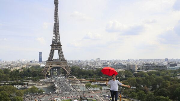 الفرنسي ناثان بولين يحمل مظلة وهو يسير، للمرة الثانية، على حبل مشدود بارتفاع 70 مترًا يمتد 670 مترًا بين برج إيفل ومسرح شايو الوطني، كجزء من أيام التراث الأوروبي الـ 38 وإطلاق الأولمبياد الثقافي في باريس، فرنسا 19 سبتمبر 2021. - سبوتنيك عربي