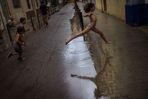 أطفال يقفزون فوق بركة من الماء وهم يلعبون أثناء عاصفة ممطرة في أحد شوارع برشلونة، إسبانيا، 18 سبتمبر 2021. - سبوتنيك عربي