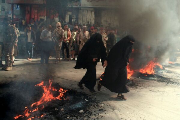 نساء يمرون بجوار إطارات محترقة خلال احتجاجات على تدهور الوضع الاقتصادي وانخفاض قيمة العملة المحلية في تعز، اليمن، 27 سبتمبر 2021. - سبوتنيك عربي