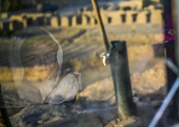طفلة من هزارة تنظر من خلف زجاج بيتها الحجري في قرية باميان، أفغانستان 3 أكتوبر2021 - سبوتنيك عربي