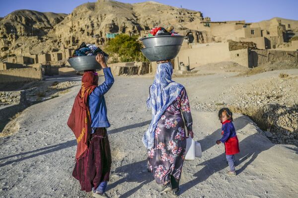 نساء، من هزارة، يحملن الملابس المغسولة يتوجهن إلى منازلهن في قرية بالقرب من جرف صخري في باميان، أفغانستان 3 أكتوبر2021 - سبوتنيك عربي
