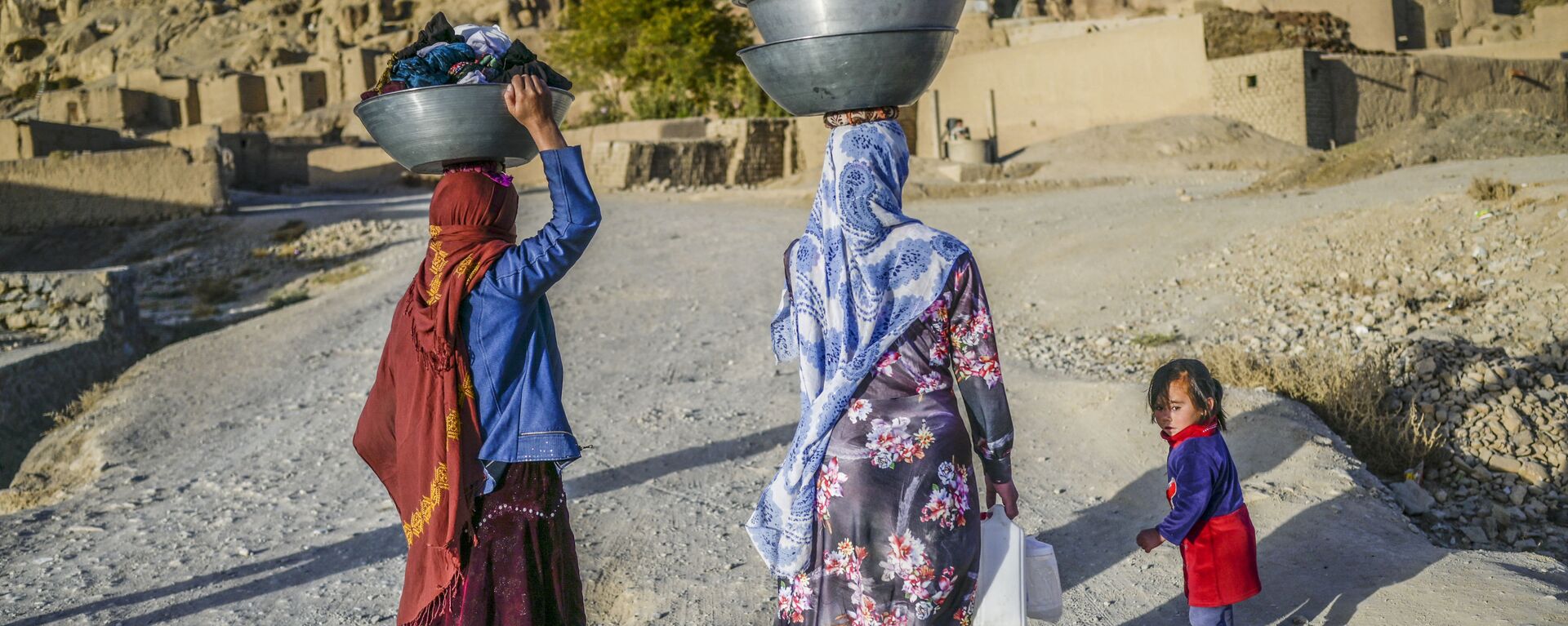نساء، من عرقية هزارة، يحملن الملابس المغسولة يتوجهن إلى منازلهن في قرية بالقرب من جرف صخري في باميان، أفغانستان 3 أكتوبر2021 - سبوتنيك عربي, 1920, 05.10.2021