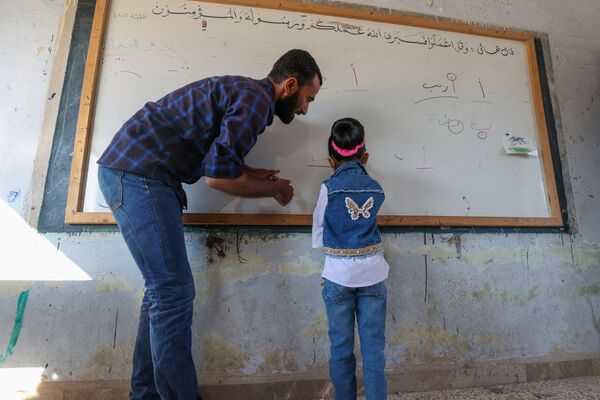 مدرس يساعد تلميذة صغيرة في اليوم الأول من المدرسة في قرية بريف إدلب شمال غرب سوريا، 9 أكتوبر 2021. - سبوتنيك عربي