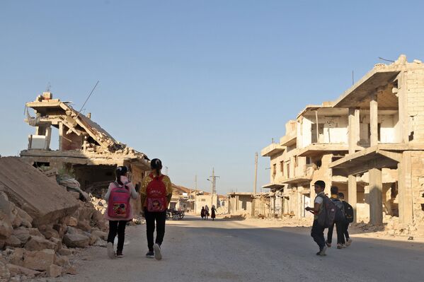 أطفال يمشون بين الأنقاض أثناء حضورهم اليوم الأول من المدرسة في قرية في ريف إدلب شمال غرب سوريا، 9 أكتوبر 2021. - سبوتنيك عربي
