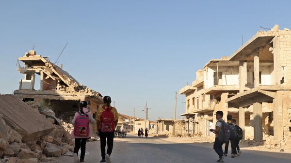أطفال يمشون بين الأنقاض أثناء حضورهم اليوم الأول من المدرسة في قرية في ريف إدلب شمال غرب سوريا، 9 أكتوبر 2021.  - سبوتنيك عربي