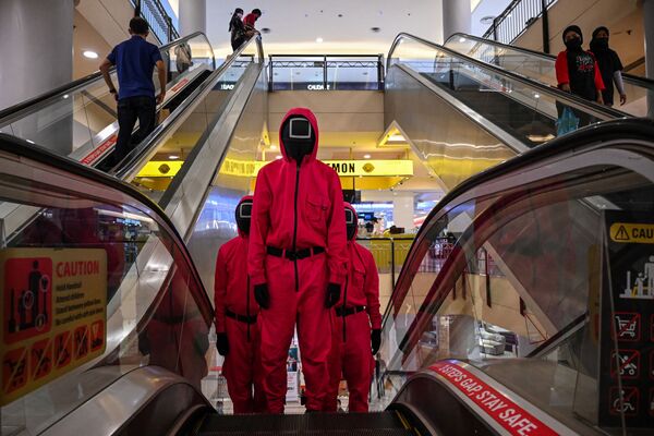 فنانون يرتدون ملابس شخصيات من مسلسل لعبة الحبار الذي اشتهر على شبكة نتفليكس، يظهرون على سلم متحرك في أحد مراكز التسوق في مدينة كوالالمبور، ماليزيا 20 أكتوبر 2021. - سبوتنيك عربي