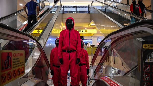 فنانون يرتدون ملابس شخصيات من مسلسل لعبة الحبار الذي اشتهر على شبكة نتفليكس، يظهرون على سلم متحرك في أحد مراكز التسوق في مدينة كوالالمبور، ماليزيا 20 أكتوبر 2021. - سبوتنيك عربي