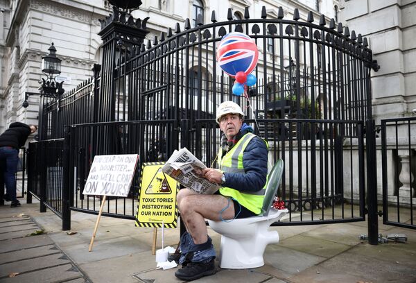 الناشط ستيف براي، يتظاهر جالساً على مرحاض خارج بوابات داونينغ ستريت، بعد تصويت أعضاء البرلمان البريطاني ضد مشروع قانون البيئة، مما يسمح للشركات بضخ مياه الصرف الصحي الخام في الأنهار والبحار في المملكة المتحدة، لندن، بريطانيا، 26 أكتوبر 2021. - سبوتنيك عربي