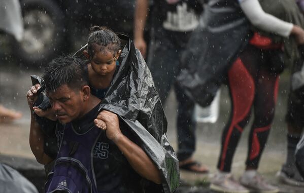 مهاجر يحمل طفلًا صغيرًا والمطر الغزير يتساقط عليهما، متجهين نحو مكسيكو سيتي لطلب اللجوء ووضع اللاجئ في هويكستلا، ولاية تشياباس، المكسيك، 25 أكتوبر 2021. - سبوتنيك عربي