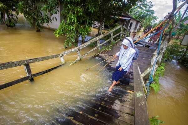 طالبة تحاول السير على جسر مكسور، الذي تعرض لمجرى فيضان النهر في قرية جارانيه، وسط هولو سونغاي، مقاطعة كاليمانتان الجنوبية، إندونيسيا، 17 نوفمبر 2021 - سبوتنيك عربي