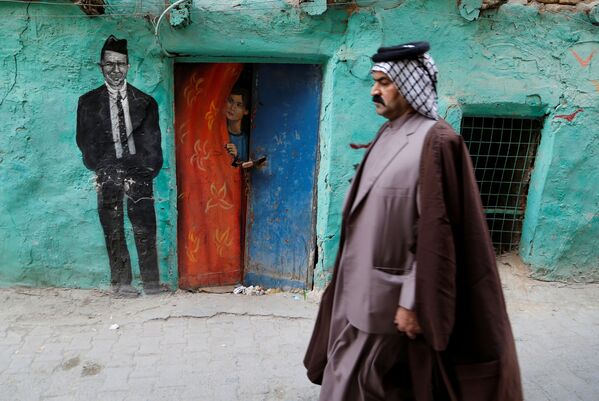 رجل يمشي أمام لوحة جدارية رسمتها مجموعة من الرسامين العراقيين الذين تطوعوا لطلاء جدران منازل الأحياء القديمة لتزيين مدينتهم، في حي الكاظمية في بغداد، العراق، 30 نوفمبر 2021 - سبوتنيك عربي