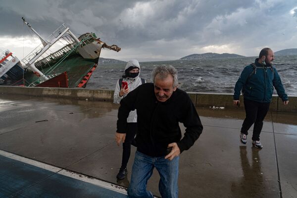 أشخاص يسيرون بالقرب من قارب انقلب بسبب الرياح العاتية في اسطنبول، تركيا، الثلاثاء 30 نوفمبر 2021 - سبوتنيك عربي
