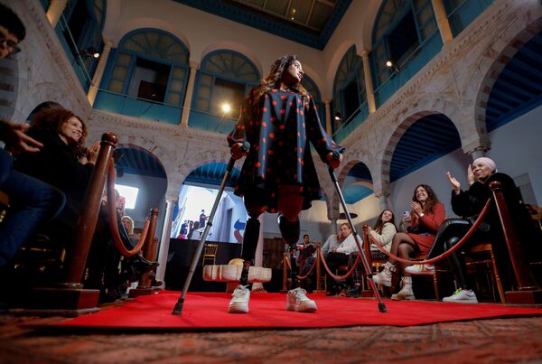 امرأة بأرجل اصطناعية تمشي على عكازين خلال عرض أزياء يهدف إلى محاربة المفاهيم الخاطئة حول معايير الجمال وتمكين النساء والفتيات، في سيدي بوسعيد، بالقرب من تونس العاصمة، 27 نوفمبر 2021 - سبوتنيك عربي