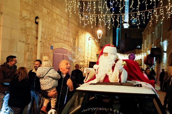 فلسطيني يرتدي زي سانتا (بابا نويل) يتفاعل مع أحد المارة  خلال احتفال مع بداية موسم مهرجان عيد الميلاد في بيت لحم بالضفة الغربية المحتلة، 2 ديسمبر 2021 - سبوتنيك عربي