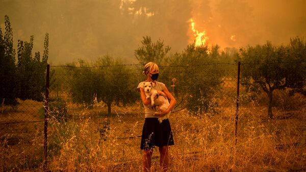 امرأة تحمل كلبًا بين ذراعيها مع اقتراب حرائق الغابات من قرية بيفكي في جزيرة إيفيا، ثاني أكبر جزيرة في اليونان، 8 أغسطس 2021. - سبوتنيك عربي
