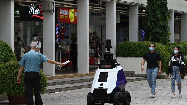 في هذه الصورة التي التقاطت في 6 سبتمبر 2021، يشير رجل إلى روبوت مستقل يُدعى خافيير (Xavier) أثناء قيامه بدوريات في منطقة التسوق والسكن خلال تجربة مدتها ثلاثة أسابيع من قبل وكالة Home Team Science and Technology (HTX) في سنغافورة. - سبوتنيك عربي