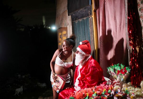 تتلقى كارولين فيتوريا، البالغة من العمر 16 عامًا، هدية من رجل يرتدي زي بابا نويل أثناء توزيعه الهدايا الممنوحة للأطفال خلال حفلة عيد الميلاد في حي سيداد دي ديوس الفقير، في ريو دي جانيرو، البرازيل، 20 ديسمبر 2021. - سبوتنيك عربي