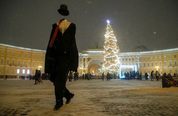 فنان يسير بالقرب من شجرة عيد الميلاد في ساحة القصر الشتوية المزينة قبل رأس السنة الجديدة وموسم عيد الميلاد وسط سان بطرسبورغ، روسيا، 23 ديسمبر 2021. - سبوتنيك عربي