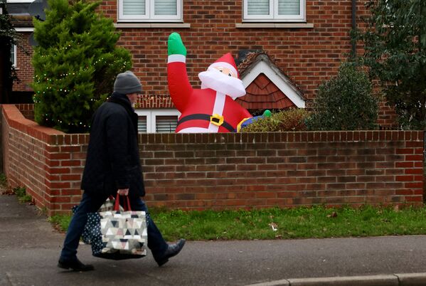 رجل يحمل أكياس تسوق يمر بجوار بالون بابا نويل المعبأ جزئيًا، في أحد أحياء لندن، بريطانيا، 20 ديسمبر 2021. - سبوتنيك عربي