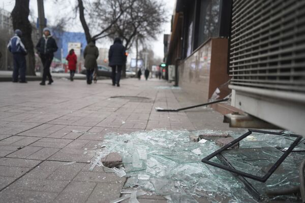 أشخاص يمشون أمام متجر به نوافذ مكسورة أثناء الاشتباكات في ألماتي، كازاخستان، 10 يناير 2022. - سبوتنيك عربي
